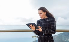 Surprised blogger girl is looking at planshet computer in hand against the background of city view.